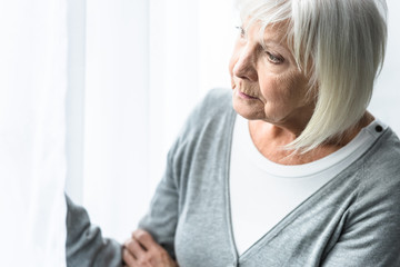 pensive senior woman with grey hair looking away at home