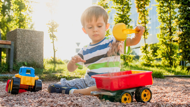 Closeup image of cute little boy playing on the palyground with toys. Child having fun with truck, excavator and trailer. He is pretending to be a builder or driver