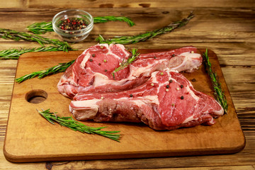 Raw fresh beef rib eye steaks on bone with spices and rosemary on wooden table