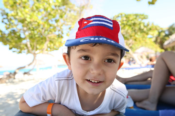 Fototapeta premium Portrait of a happy little boy in a bright red cap on his head on the beach in the Caribbean. Summer, rest, vacation, holidays
