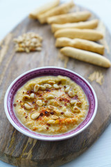 Hummus topped with pine nuts, chili flakes and olive oil, served with bread sticks. Violet bowl, wooden board, high resolution