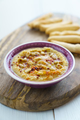 Hummus topped with pine nuts, chili flakes and olive oil, served with bread sticks. Violet bowl, wooden board, high resolution