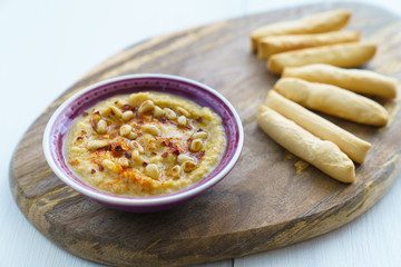 Hummus topped with pine nuts, chili flakes and olive oil, served with bread sticks. Violet bowl, wooden board, high resolution