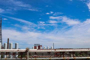 View of a pipeline overpass with pipes, columns of tanks against a blue sky with clouds at an industrial chemical refinery petrochemical plant
