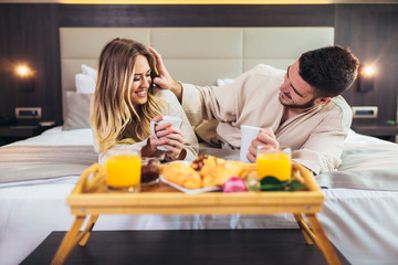 Obraz na płótnie Canvas Young happy couple having breakfast in luxury hotel room.