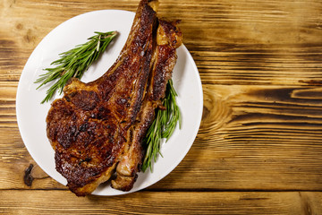 Roasted beef rib eye steak on bone with rosemary in white plate on wooden table