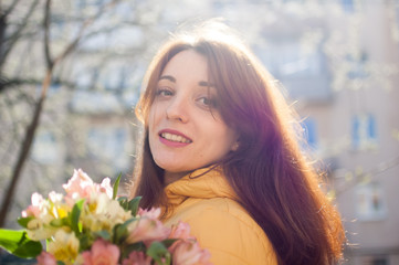 Outdoors female portrait of attractive brunette girl in yellow jacket holding a big bouquet of...