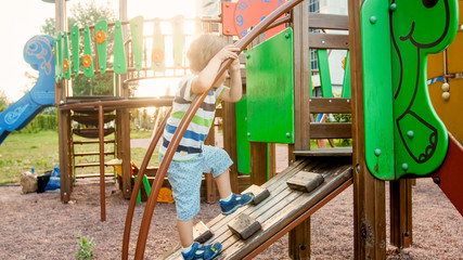 Portrait of adorable 3 years old boy climbing on ladder on the children palyground at park