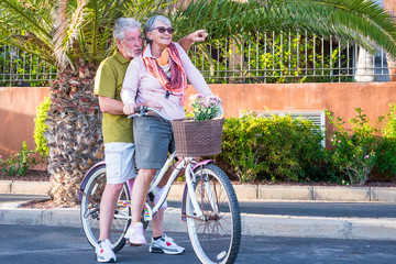 Old senior people couple enjoy retired lifestyle riding together the same coloured bike in outdoor...