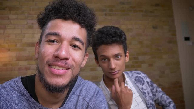 Closeup shoot of two young african american and indian male bloggers streaming live talking on camera cheerfully indoors