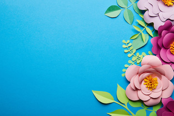 top view of colorful paper cut flowers with green leaves on blue background with copy space