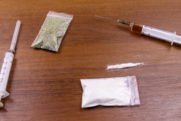 Different type of drugs: cocaine, heroin syringe and dried cannabis on a table. Drug use, crime and addiction concept