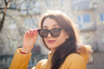 Pretty female model with sensual lips in yellow jacket wearing dark fashionable sunglasses.
