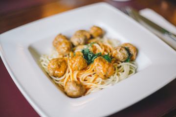 Close-up of spaghetti pasta with meatballs and tomato sauce in a white plate on the table in a restaurant