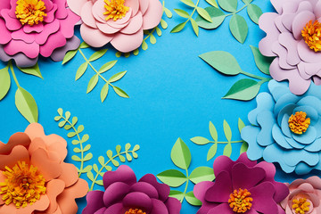 top view of multicolored paper cut flowers with leaves on blue background with copy space