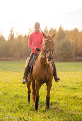 portrait of young woman riding red horse in autumn field