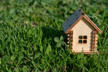 Toy wooden house on the bright grass in sunny weather. Copy space. Real estate concept, business loan financing concept, new house concept.