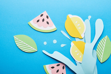 top view of paper cut water splash with lemons, leaves and watermelons on blue background