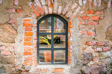 Fototapeta na wymiar Texture background, window on the wall stone house. There is a light in the window and a flower stands on the windowsill.