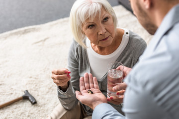 partial view of man giving to senior mother glass of water and medicine