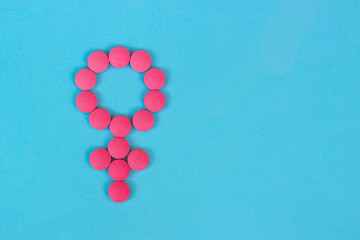 Gender symbol of woman from red pink pills on blue background top view with copy space, concept about female health.
