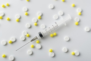 medical syringe next to yellow and white pills of medical drugs and vitamins are in the hospital on a white background