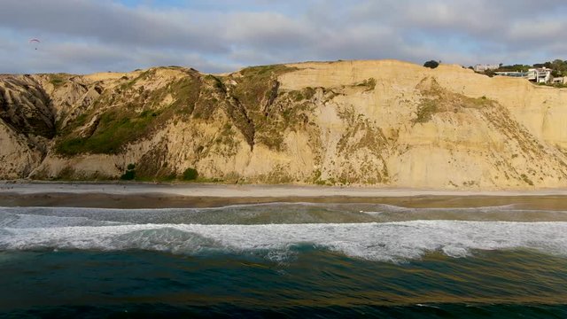 Aerial view of pacific coastline with yellow sandstone cliffs and waves rushing the beach during sunset. Black Beach, Torrey Pines State Natural Reserve, San Diego, California, USA
