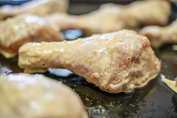 Raw chicken legs, spicy marinated legs on a baking sheet. Selective focus on one raw chicken leg.