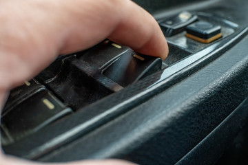 Close up male driver's hand pressing car window controls button.