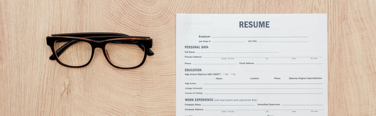panoramic shot of resume template and glasses on wooden surface
