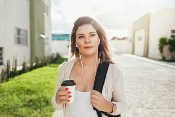 Female student dressed in casual clothing walking around the city and listening to music via earphones