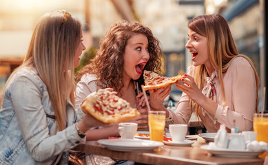 Three cheerful girls eating pizza in a outdoor restaurant