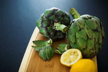 Fresh artichokes on wooden cutting board with lemons