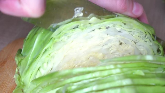 female hands cut green cabbage cabbage on a wooden surface of a kitchen table, close-up