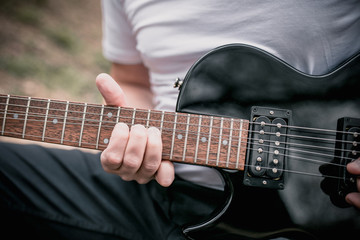 Fototapeta na wymiar Left handed male playing a black left-handed electric guitar outside outdoors