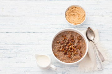 Delicious oatmeal in a white bowl, dates fruits, cocoa and vegan milk