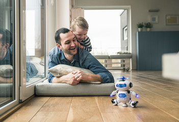 Excited father and son lying on a mattress at home watching a toy robot
