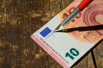 ten euros on a wooden background. The pen of a fountain pen is enclosed in a signature on a banknote. Concept - fake money