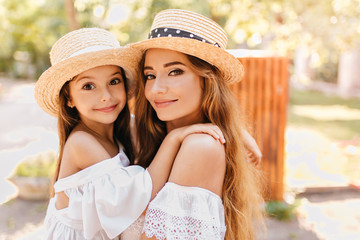 Beautiful young woman with big green eyes holding daughter wich looking to camera with surprised...