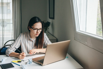 A young beautiful student girl does homework or writes a to-do list or this girl works in a home office. Home education or business or planning.