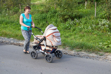 a woman laughs with a baby stroller,happy woman walking on the road with a stroller in the summer