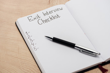 notebook with exit interview checklist lettering and numbers on wooden table with pen