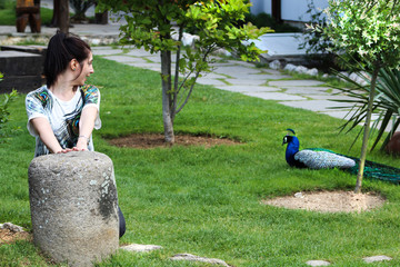 Woman watching peacock in the middle of the meadow  
