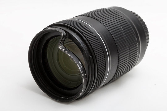 Damaged and broken zoom lens for the digital camera, dented protective UV filter. Front side closeup view. To be repaired. Isolated on white background