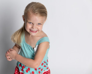 Young girl with blonde hair and blue eyes in flower print dress against white background