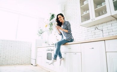 Beautiful cute smiling woman is using smart phone on the kitchen at home.