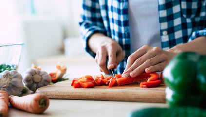 Female hands is cutting peppers for salad on the table in kitchen.