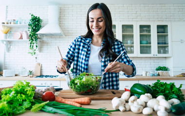 Beautiful cute young smiling woman on the kitchen is preparing a vegan salad in casual clothes.