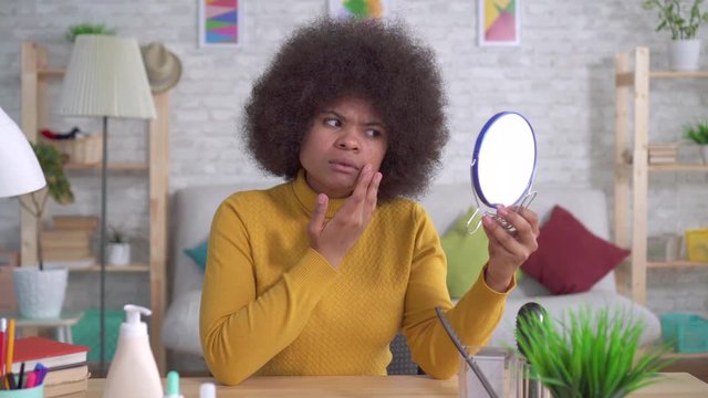 portrait african american woman with an afro hairstyle of that unhappy looking in the mirror finds a defect in the skin