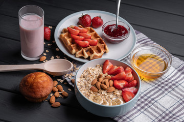 Crispy waffle with milk oatmeal with fruit for breakfast. Healthy food. Vegan dishes. Chocolate muffin and berry yogurt. On a black background